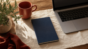 Editorial flat-lay of a passport-style navy travel document beside a laptop and terracotta mug on cream linen — Canada online passport renewal