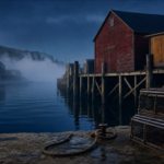 Newfoundland fishing wharves with brick-red and ochre fishing sheds at blue hour, mooring rope and lobster traps on a stone pier — editorial photograph illustrating Atlantic Canada immigration to Newfoundland and Labrador